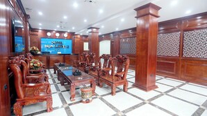A hotel conference room with wooden furniture, a large TV screen, and a patterned wall. - Hoa Cương Hotel 2 (Ha Giang 1)
