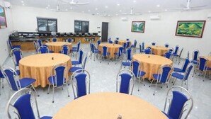 A conference room with round tables and blue chairs, a kitchen area, and ceiling fans. - Hoa Cương Hotel 2 (Ha Giang 1)