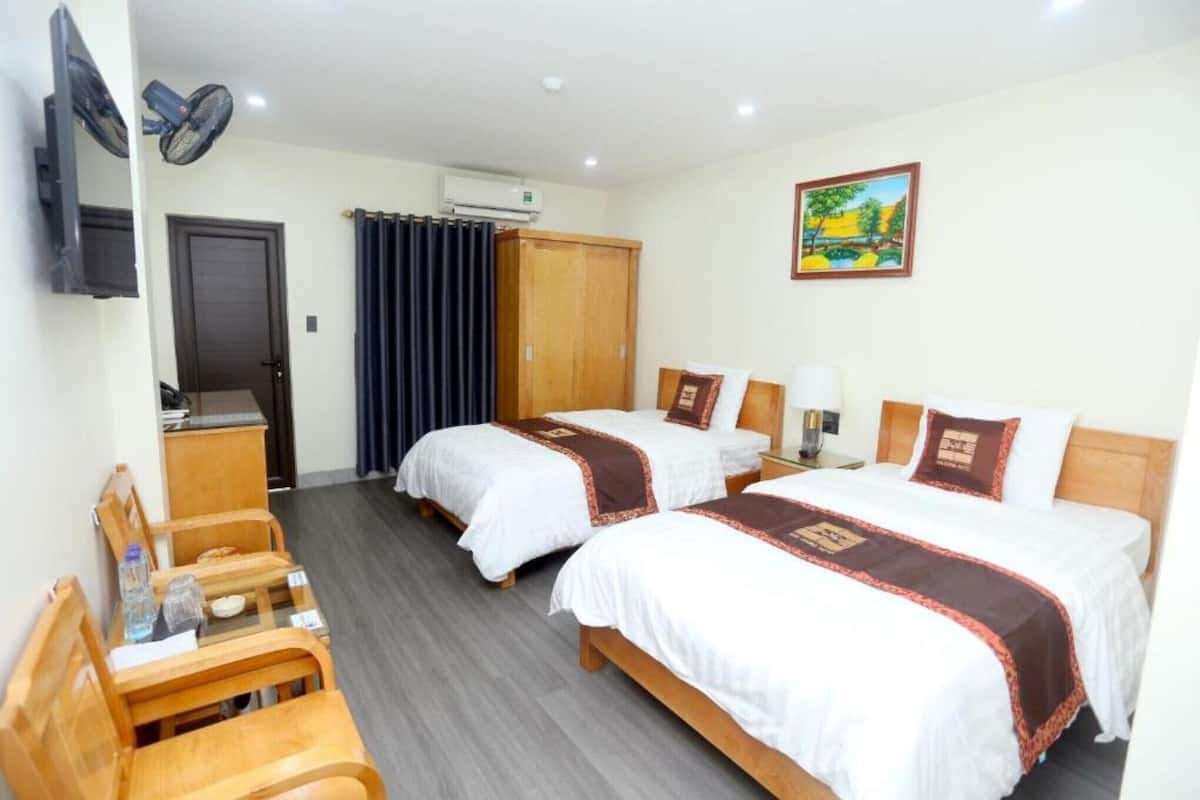 Habitación de hotel con dos camas, un escritorio, una silla, un televisor, un armario y un cuadro en la pared.