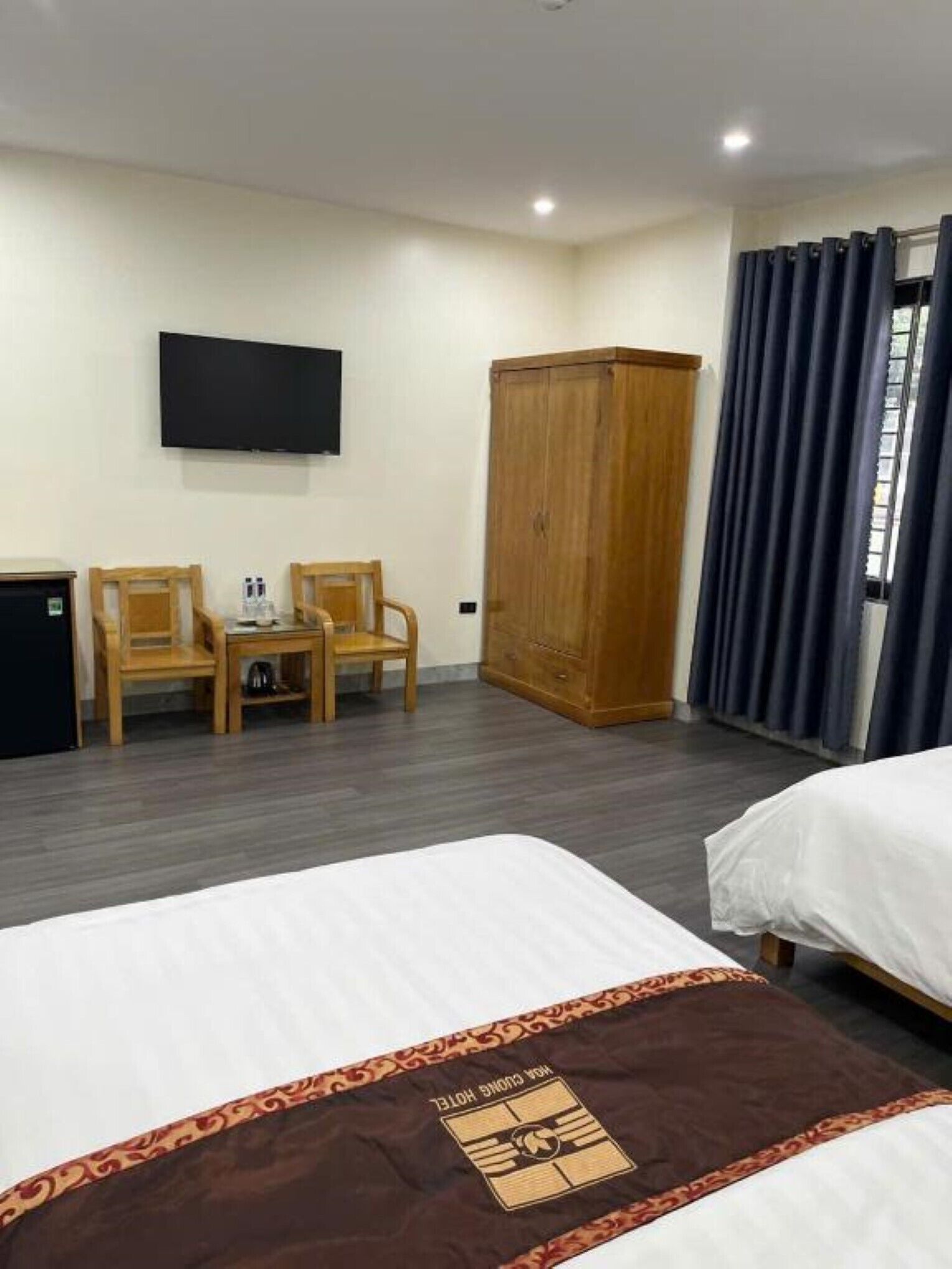 A hotel room with two beds, a TV, a wardrobe, and a desk with chairs.