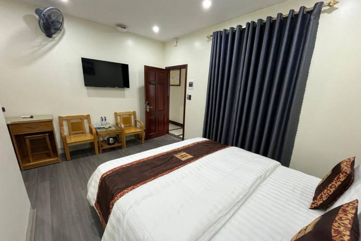 Una habitación de hotel con una cama, un escritorio, dos sillas, un televisor y una puerta.