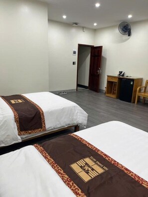 A hotel room with two beds, a desk, a chair, and a wall-mounted fan. - Hoa Cương Hotel 2 (Ha Giang)
