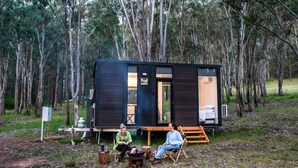 Una cabaña con terraza de madera, un pequeño espacio de estar al aire libre y una vista despejada del bosque circundante.