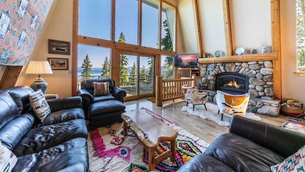 A spacious living room with leather sofas, a stone fireplace, and large windows offering a view of trees and mountains. - 4BD w/Lake Views - Near Beach and Slopes (Tahoe City)