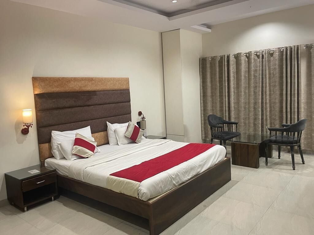 A modern hotel room with a large bed, bedside tables, a desk, and two chairs.