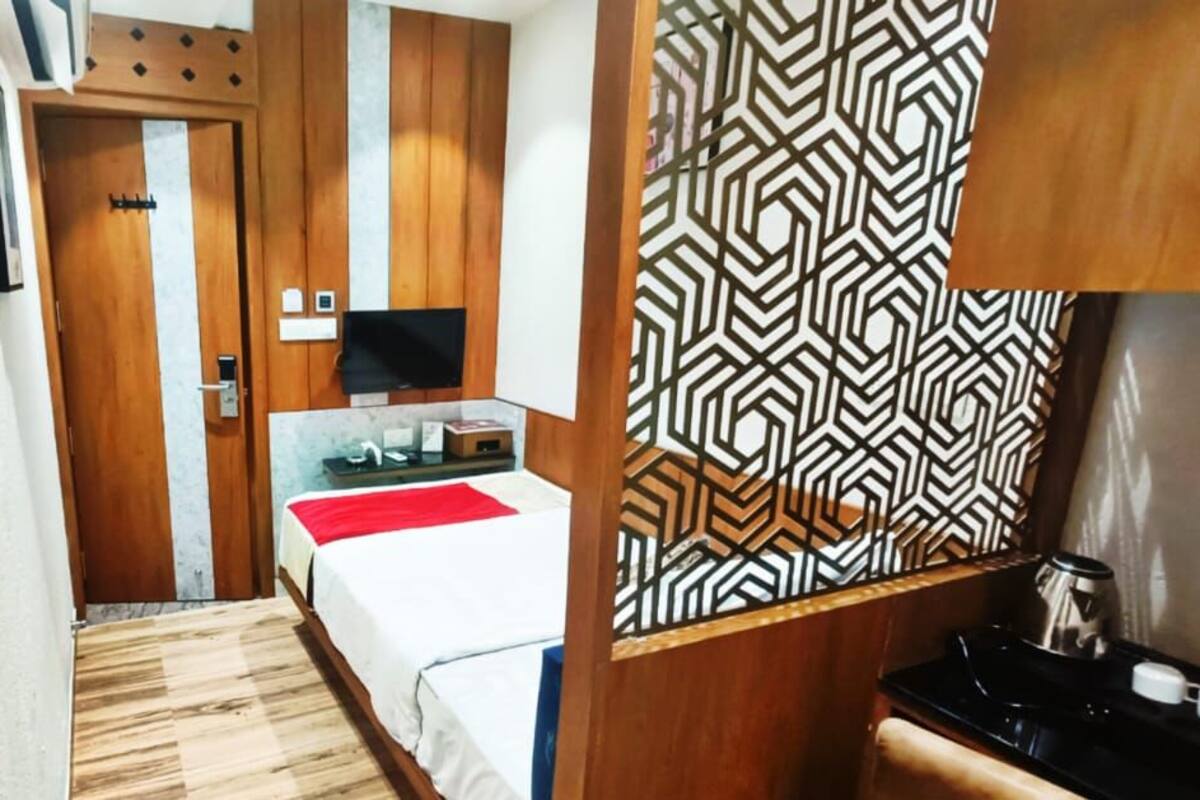 A hotel room with two beds, a TV, a small kitchenette, and a patterned wall.
