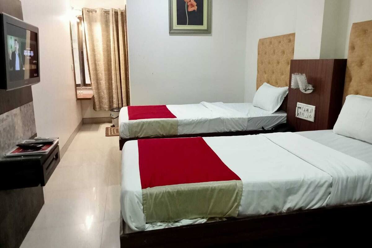 A hotel room with two beds, a television, a painting, and a curtain.