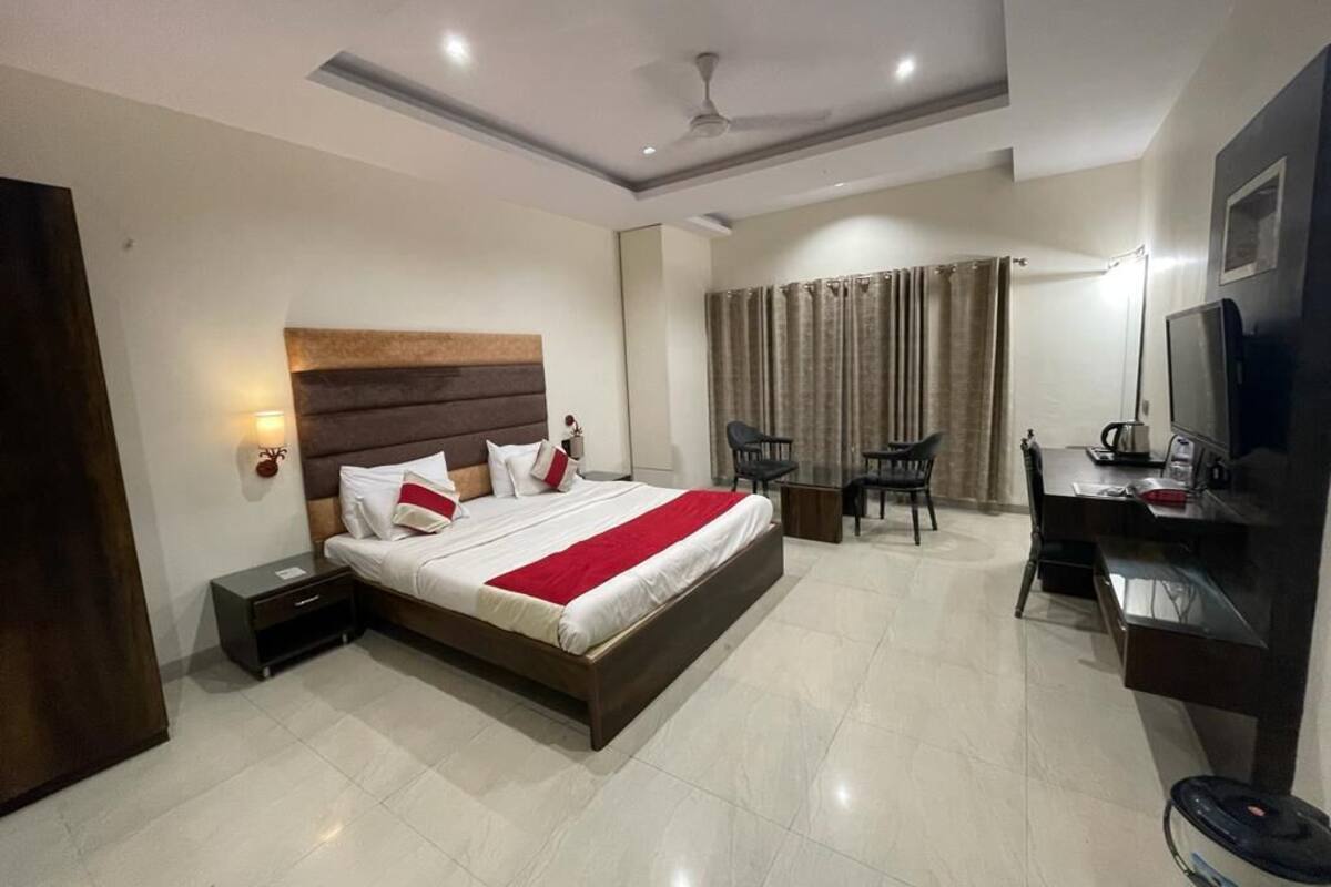 A hotel room with a bed, bedside table, desk, chair, and a television.