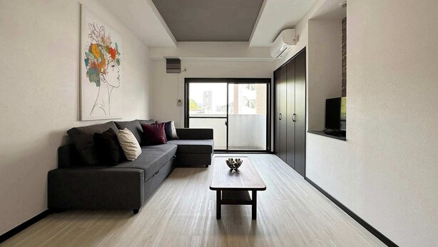 A modern living room with a grey sofa, a coffee table, and a large window with a view of buildings. - 2Br Apt for 10ppl Very Good Location (Minami Ward, Hiroshima)