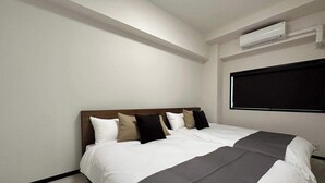 A hotel room with a large bed, a headboard, a window, and an air conditioning unit. - 2Br Apt for 10ppl Very Good Location (Minami Ward, Hiroshima)