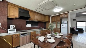 A modern kitchen with wooden cabinets, a built-in oven, and a dining area with a wooden table and chairs. - 2Br Apt for 10ppl Very Good Location (Minami Ward, Hiroshima)
