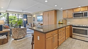 A modern kitchen with wooden cabinets, a granite countertop, and stainless steel appliances. - Walk to Beach | Pools, Pickleball, Kihei (Kihei)