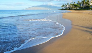 A beach with a sandy shore, ocean waves, and a mountain in the background. - Walk to Beach | Pools, Pickleball, Kihei (Kihei)