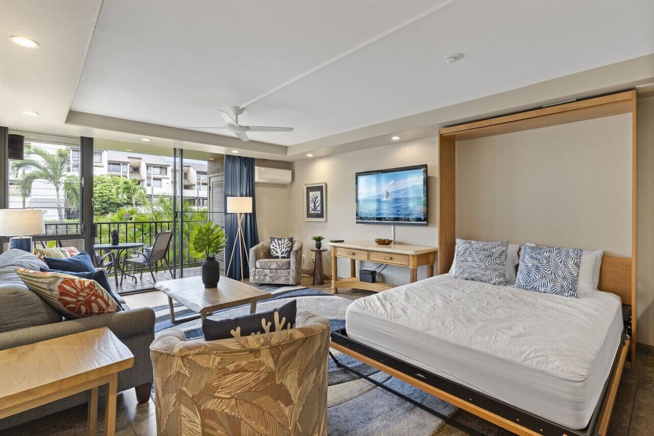 A modern hotel room with a large bed, a desk, a TV, and a balcony with a view of the city.