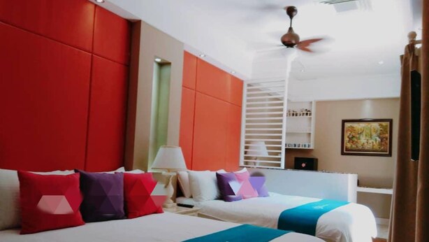 Une chambre d’hôtel avec deux lits, un ventilateur de plafond, une fenêtre avec des stores, une table de chevet avec une lampe et un tableau au mur.