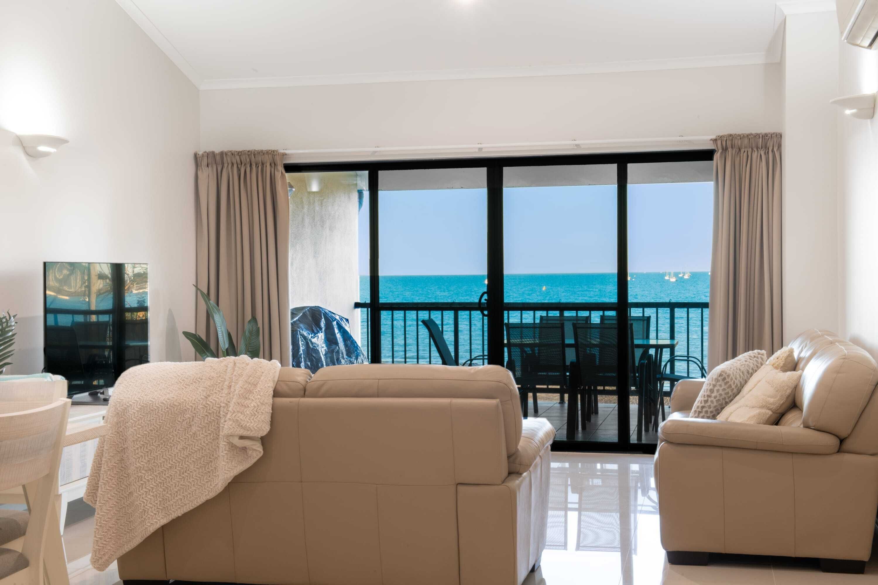 Un salon avec un canapé et un fauteuil, un téléviseur et une vue sur la mer grâce à de grandes fenêtres.
