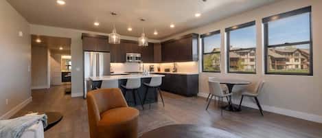 Una cocina moderna con una isla central, comedor con sillas y ventanas amplias que ofrecen vistas.