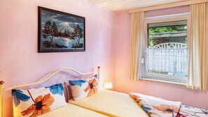 Een kamer met een bed, een raam met gordijnen, een aan de muur hangend schilderij en een bedlampje.