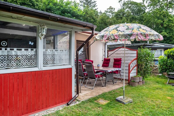 A red building with a covered patio area, a table with chairs, and an umbrella.