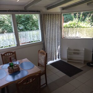 Een eethoek met een tafel, stoelen, een fles champagne en uitzicht op groen door het raam.