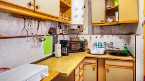 Een keuken met houten kastjes, een magnetron, een koffiezetapparaat en diverse keukengerei.
