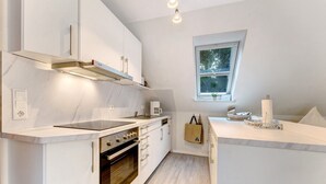 A modern kitchen with white cabinetry, a built-in oven, and a window providing natural light. - Studio Apartment 'Appartement Skagen' with Shared Garden and Wi-Fi (Glücksburg (Ostsee))