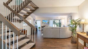 A modern living room with a wooden staircase, a grey sofa, a wooden coffee table, and a potted plant. - 2128 Beachwood (FERNANDINA BEACH)