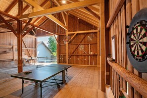 A wooden interior with a ping pong table, dartboard, and a basketball hoop.