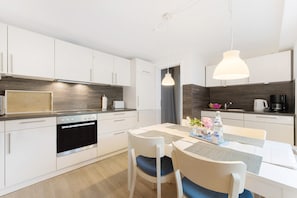 Une cuisine moderne avec des meubles blancs, un four encastré, une table à manger avec des chaises et des luminaires suspendus.