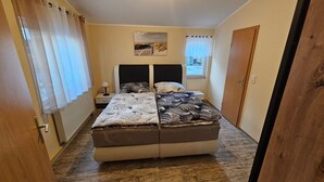 A bedroom with a bed, a nightstand, a lamp, a window with curtains, and a door.