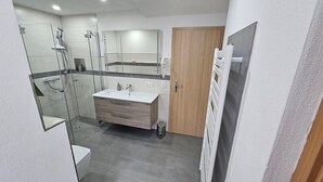 A modern bathroom with a glass shower enclosure, a vanity with a sink, and a wooden door.