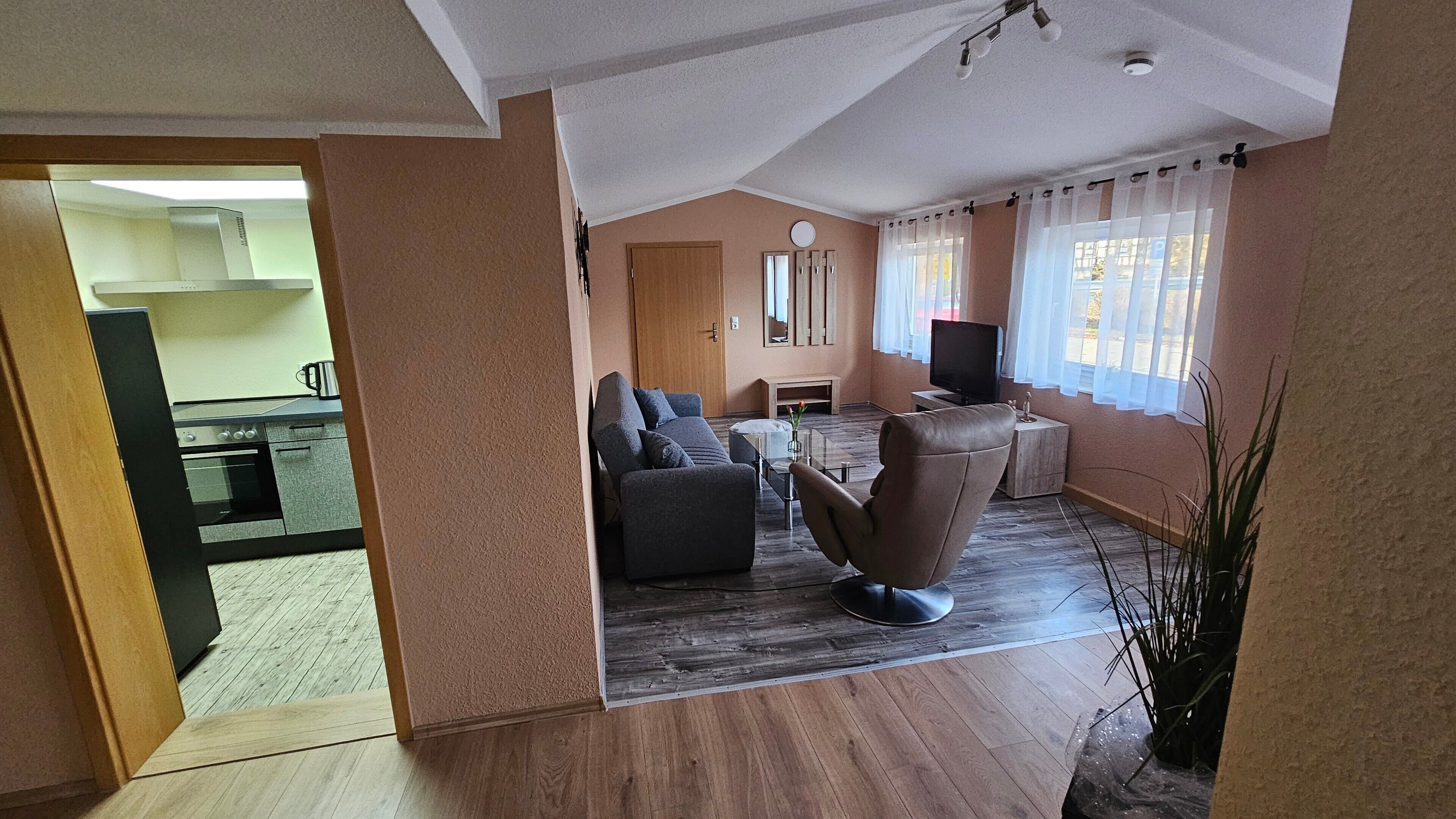 A living room with a sofa, armchair, TV, and a dining area with a table and chairs.