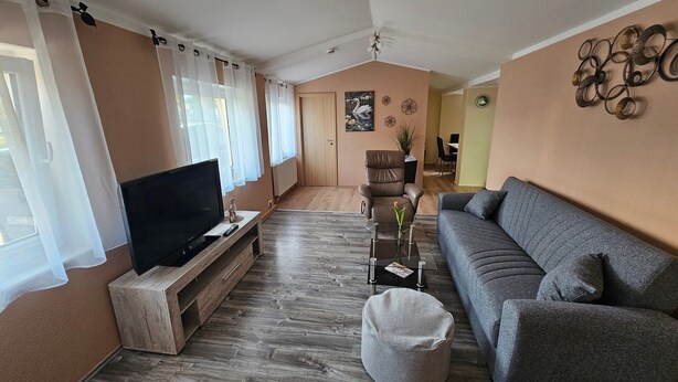 A living room with a flat-screen TV, a grey sofa, a coffee table, and a wooden TV stand.