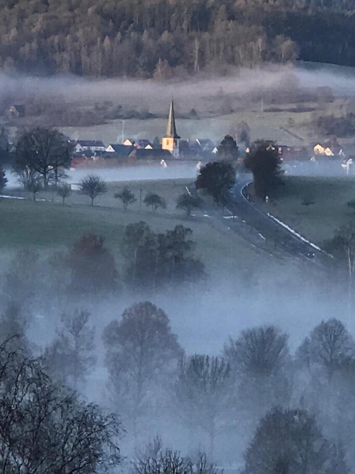 A rural landscape with a church, houses, and a road.