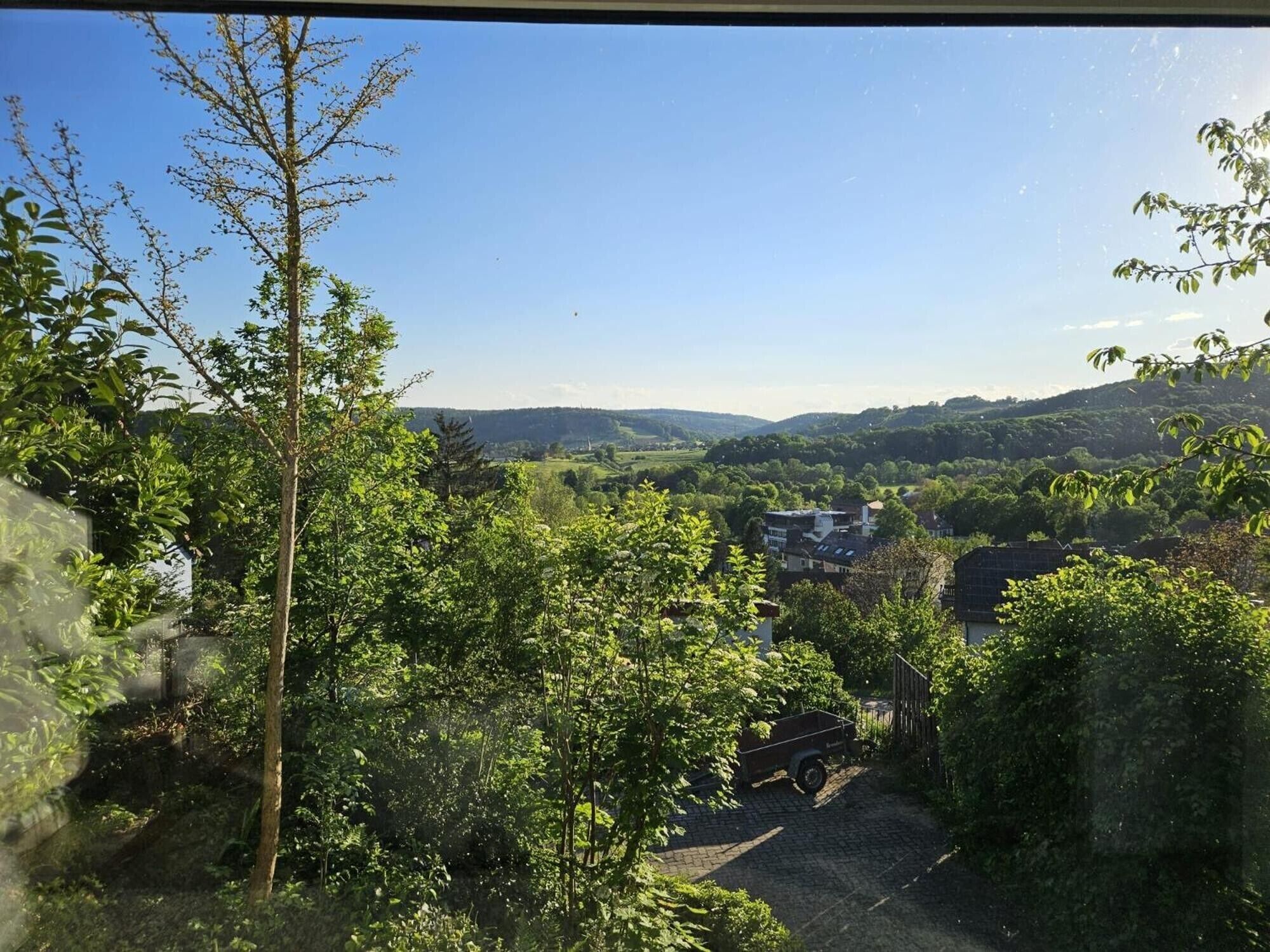 Une vue d’un paysage rural avec un chemin de terre menant à une maison entourée d’arbres.