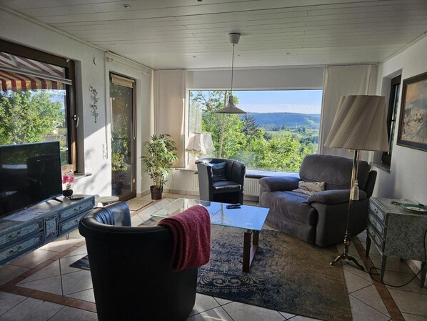 A living room with a TV, two sofas, a coffee table, and a view of the outdoors.