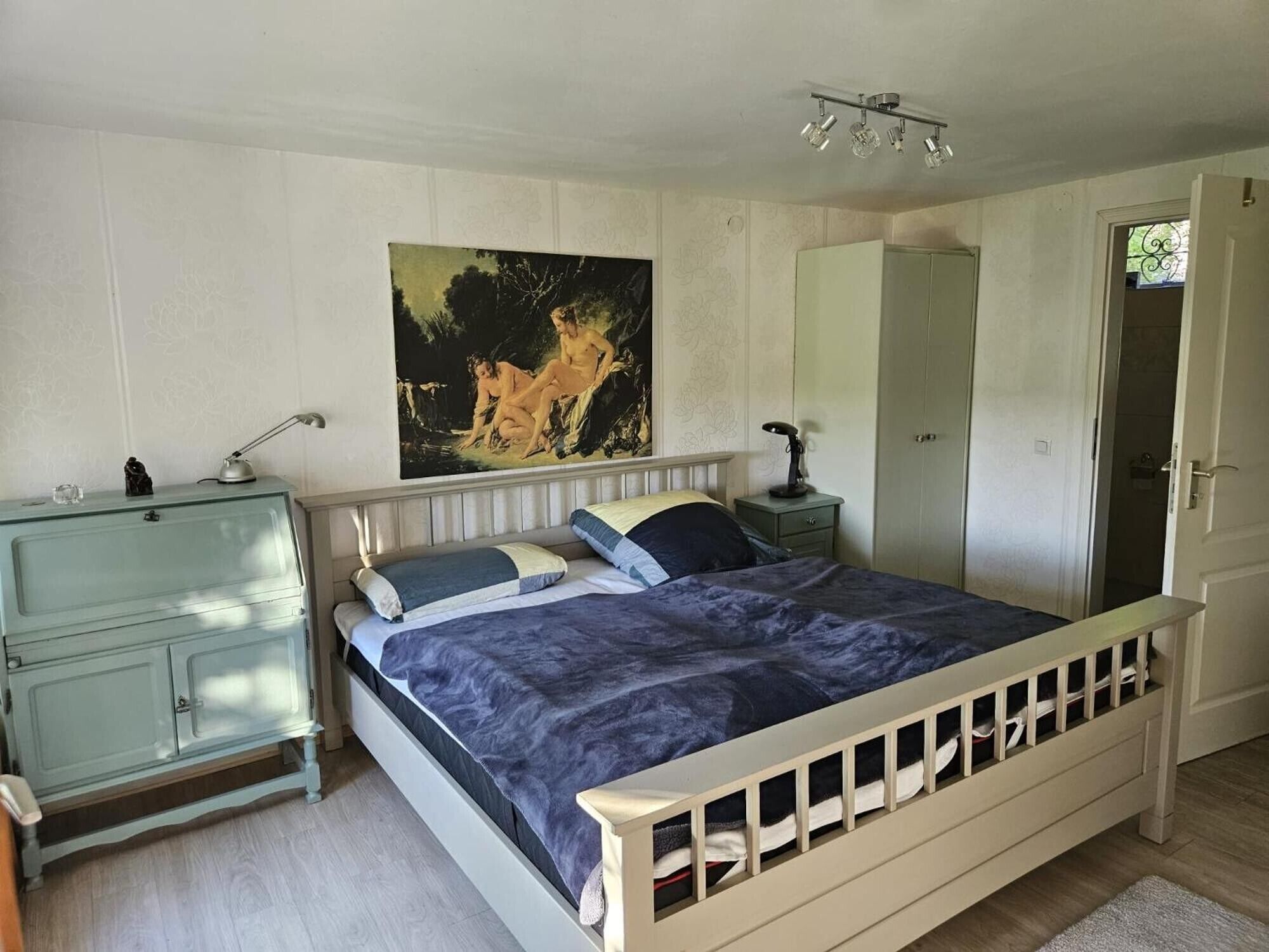 A bedroom with a bed, a dresser, a nightstand, a painting, and a wardrobe.