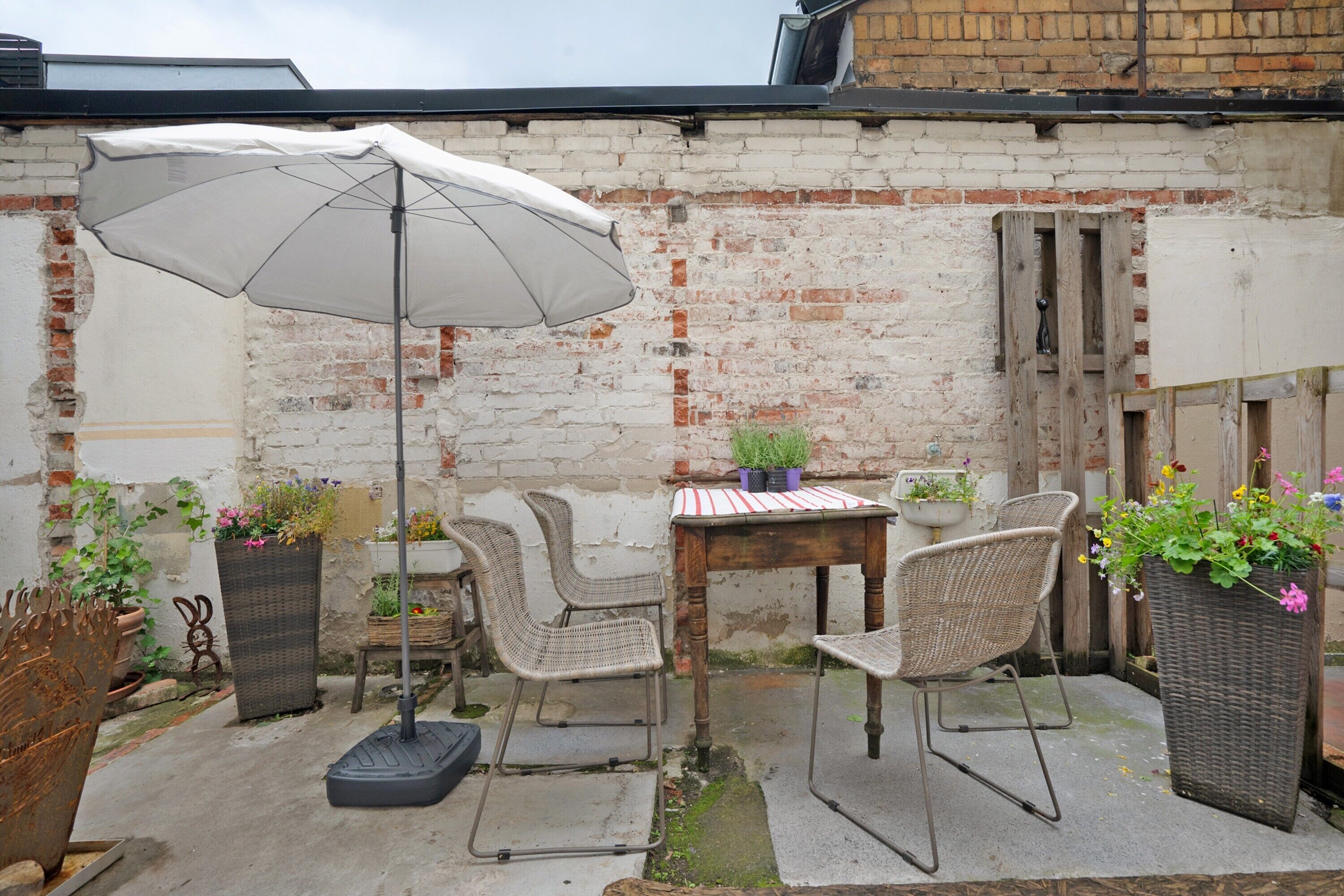 Eine Terrasse mit Tisch, Stühlen, einem Sonnenschirm und Blumentöpfen.