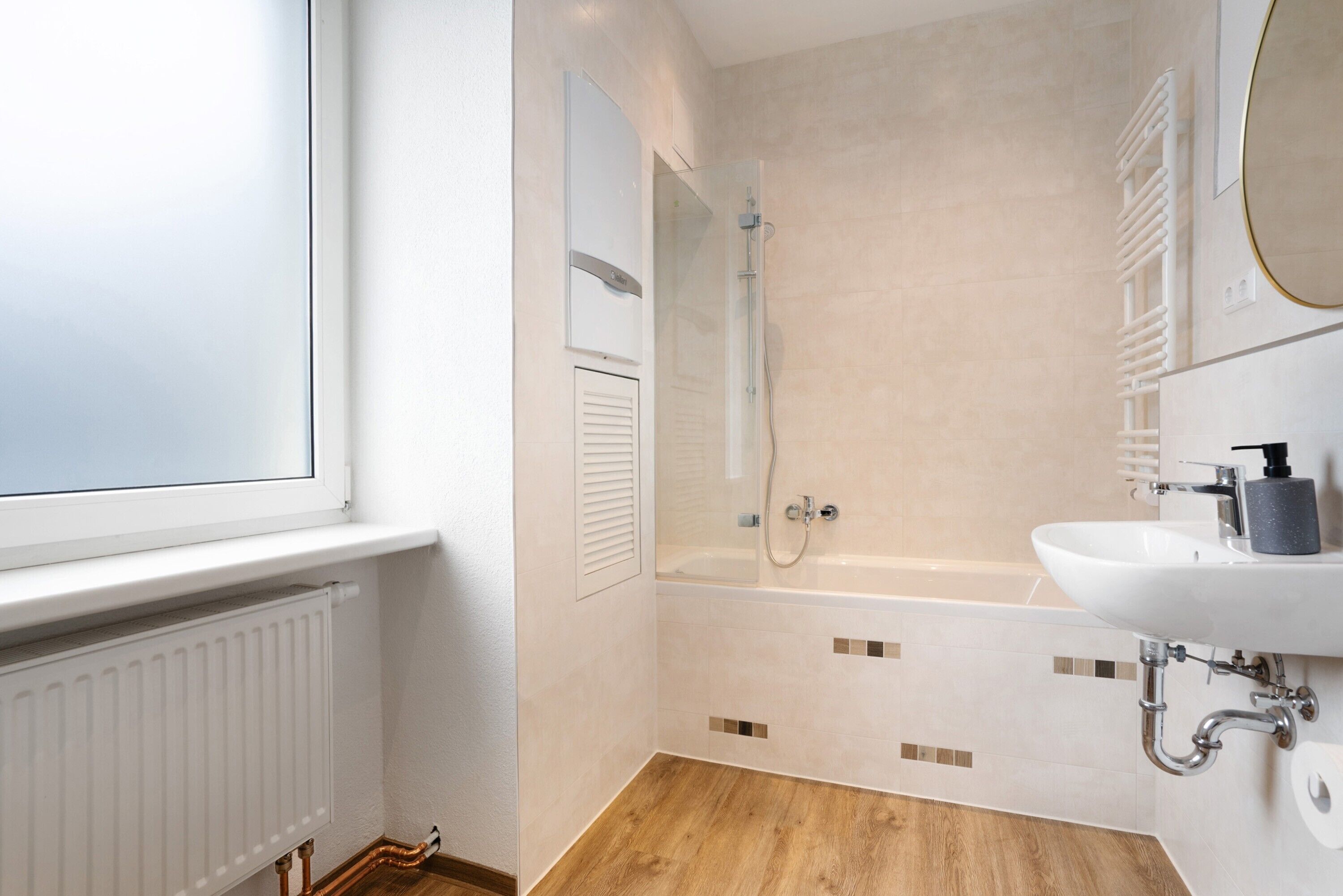 A bathroom with a bathtub, a window, a radiator, and a sink with a mirror.