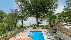 A backyard with a swimming pool, lounge chairs, and a view of a lake.