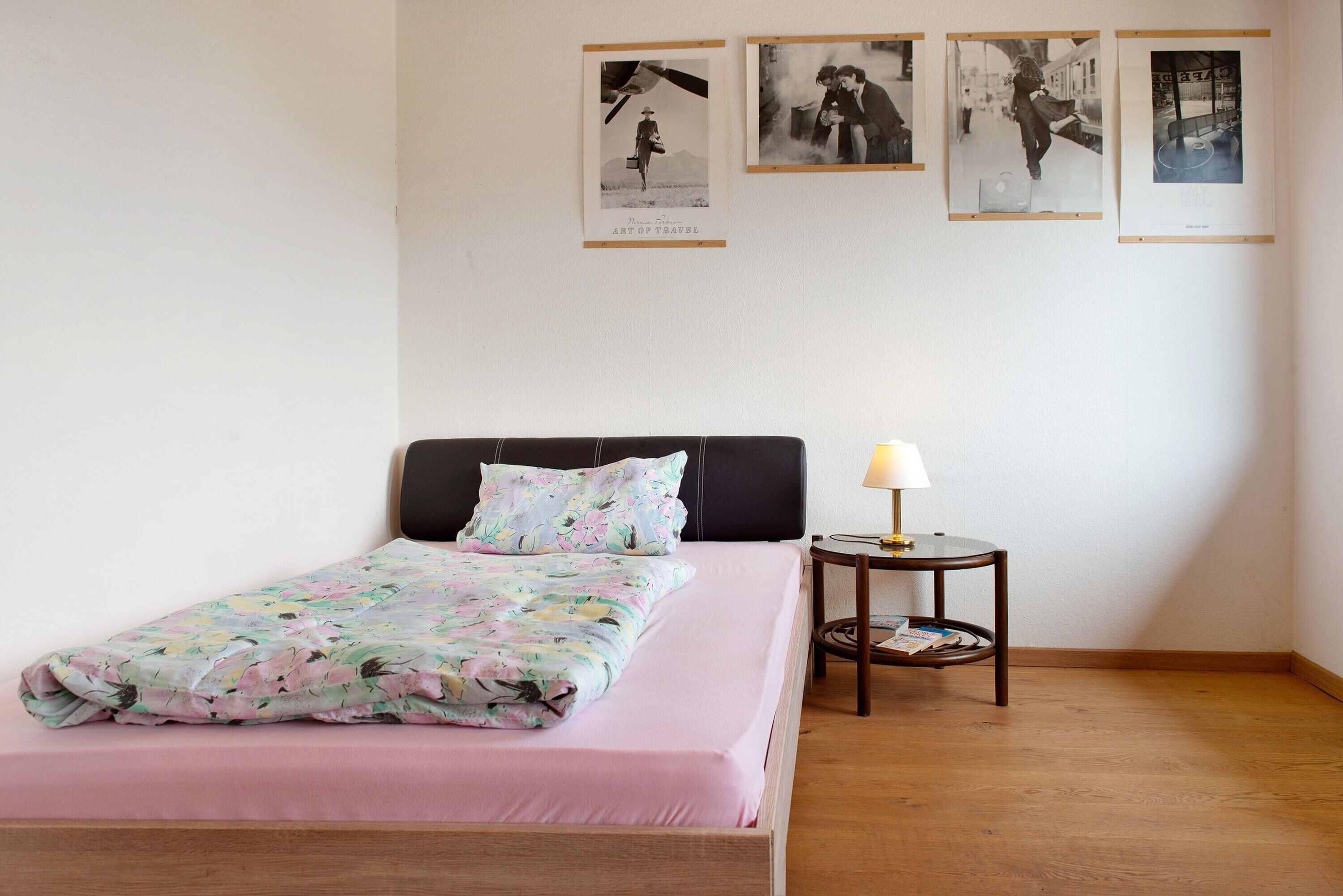 A bedroom with a bed, a nightstand, a lamp, and four framed pictures on the wall.