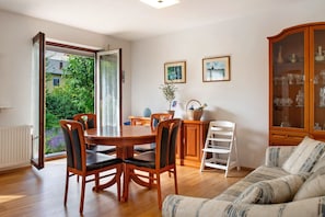 Uma área de refeições com uma mesa e cadeiras de madeira, um armário com portas de vidro e vista para o exterior arborizado.