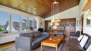 A spacious living room with a wooden ceiling, large windows, a fireplace, and a kitchen area. - Holiday Home 'Ferienhaus Christine lake constance north' with Private Terrace and Private Garden (Pfullendorf)