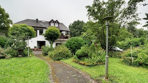 Ein Weg führt zu einem Haus mit Garten, einer Straßenlaterne und einem wolkenlosen Himmel.