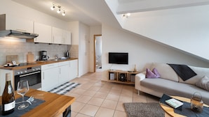 Eine moderne Küche mit Essbereich, ein Wohnzimmer mit Sofa und Fernseher sowie eine Treppe.
