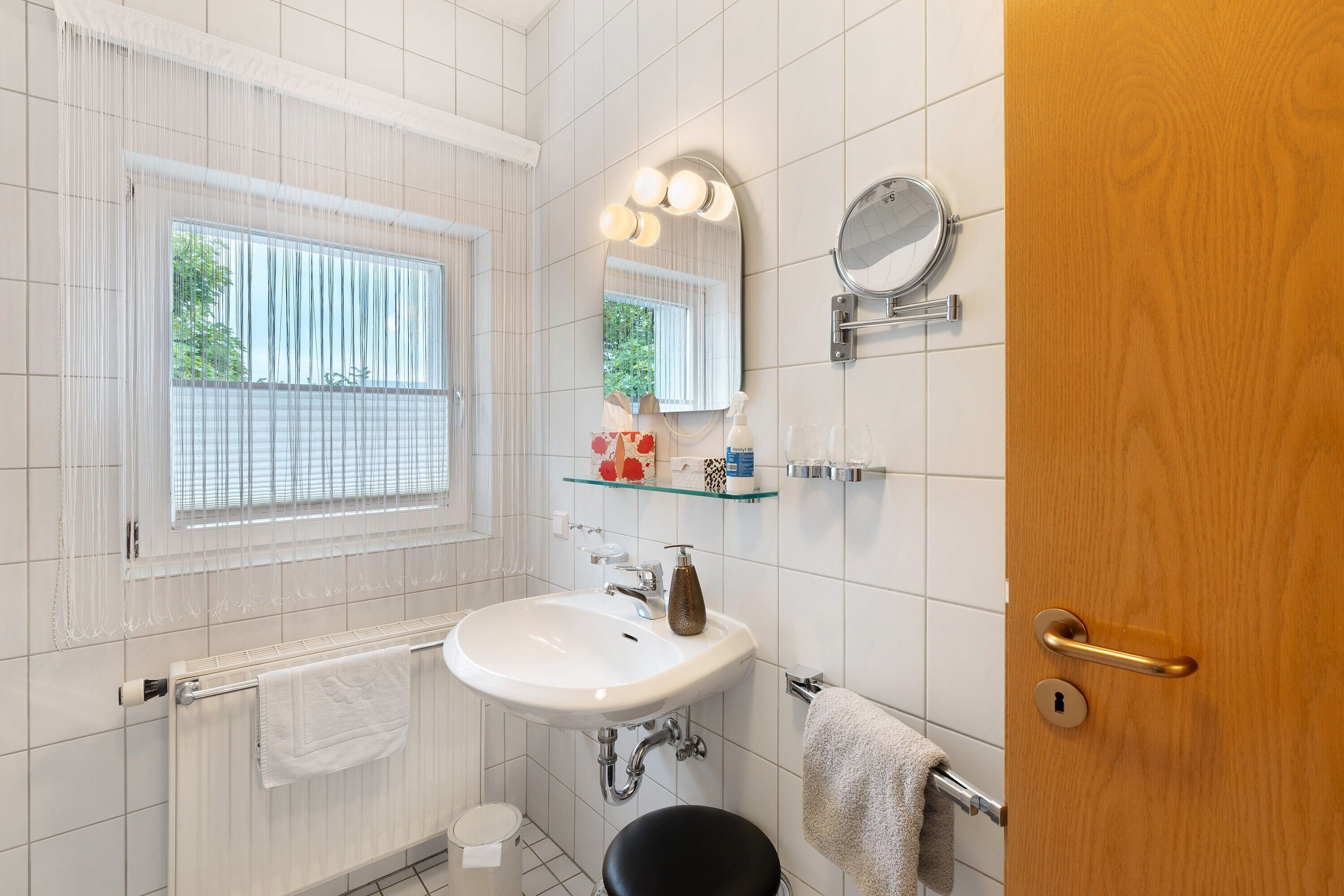 A bathroom with a white sink, a mirror, a towel rack, and a window with blinds.