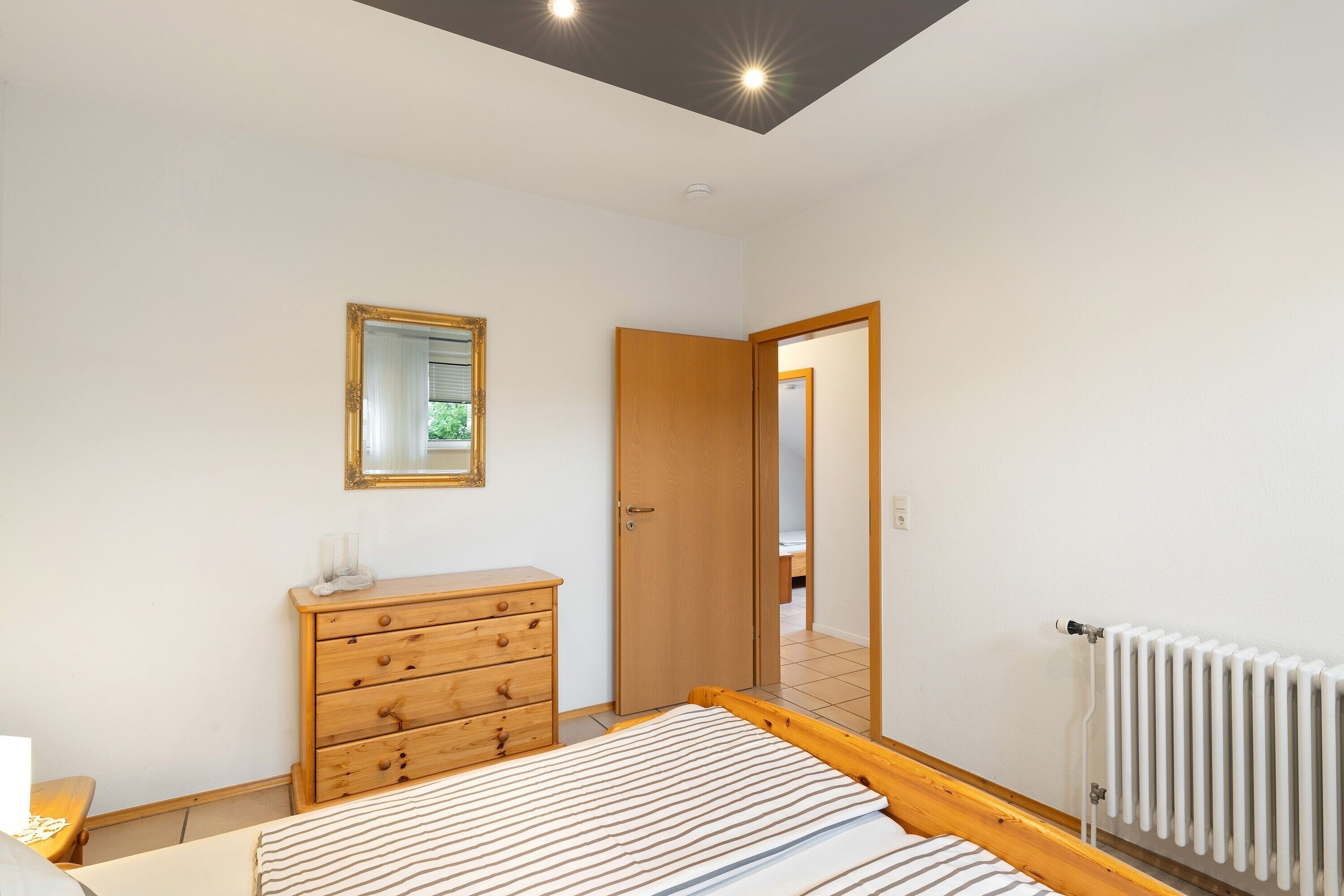 Un dormitorio con cama, cómoda de madera, espejo y radiador.