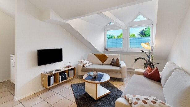Ein modernes Wohnzimmer mit Flachbildfernseher, einer Couch, einem Couchtisch und einem Bücherregal.