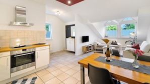 Eine moderne Küche mit Einbauofen und Herd, ein Essbereich mit Tisch und Stühlen sowie ein Wohnzimmer mit Sofa und Fernseher.