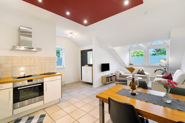 Une cuisine moderne dotée d’un four et d’une cuisinière encastrés, un coin repas avec une table et des chaises, et un salon avec un canapé et un téléviseur.